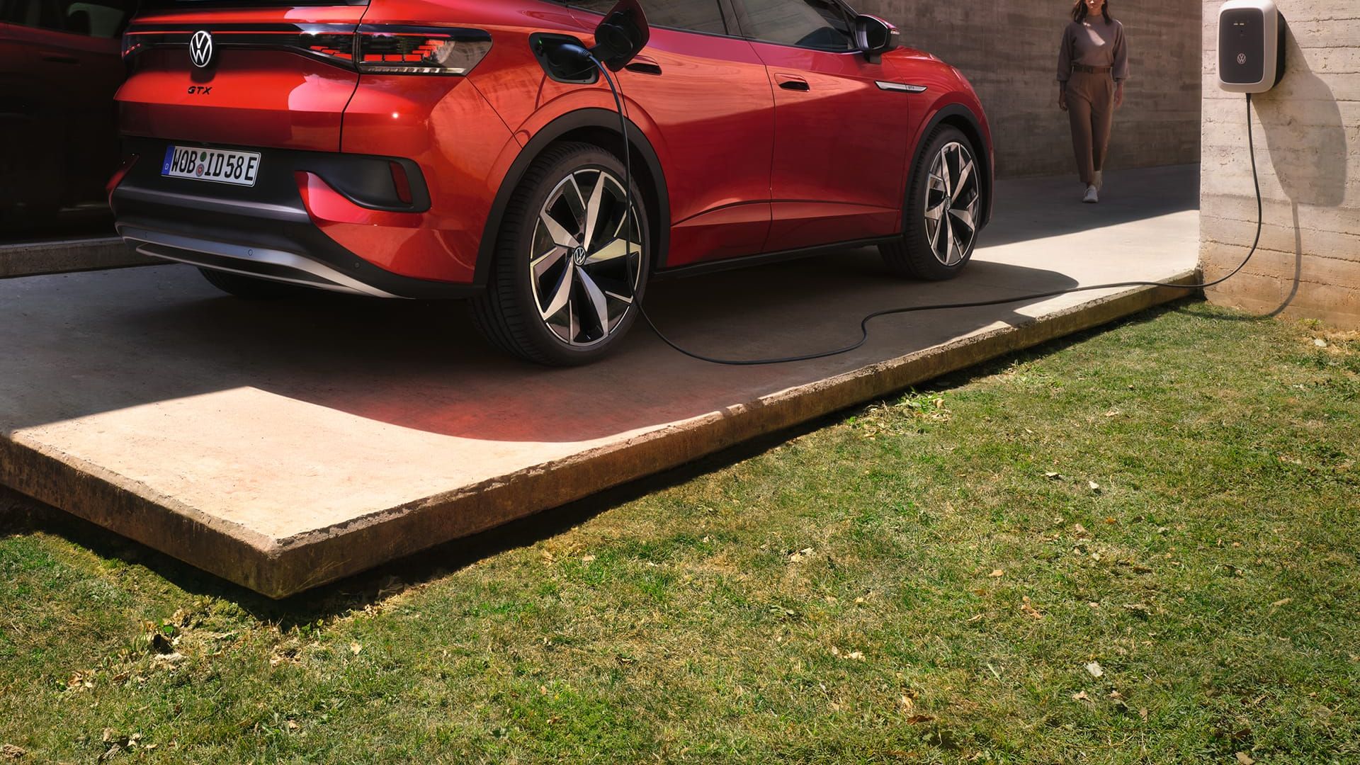 VW ID.5 GTX in Rot steht vor einem modernen Haus und lädt an einem ID. Charger, ein Mann geht auf das Auto zu