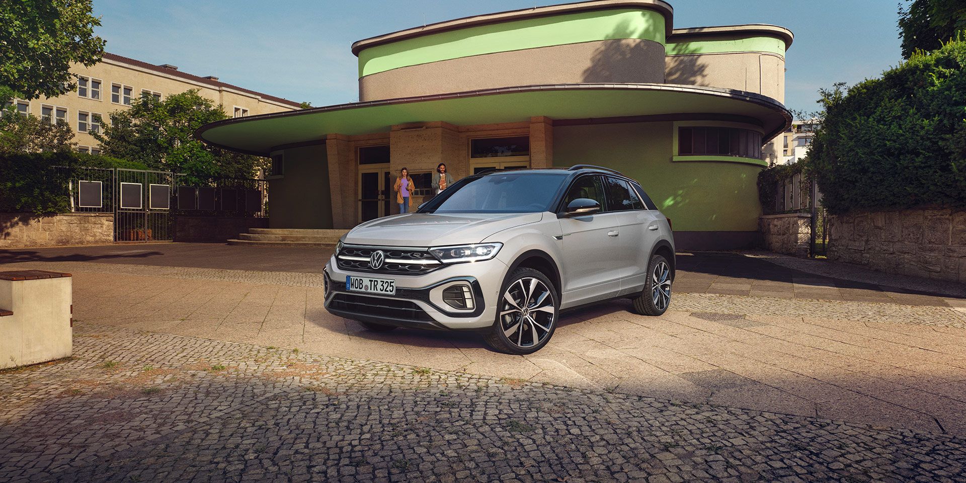VW T-Roc R-Line in weiß vor einem Gebäude, Front und Seite sichtbar