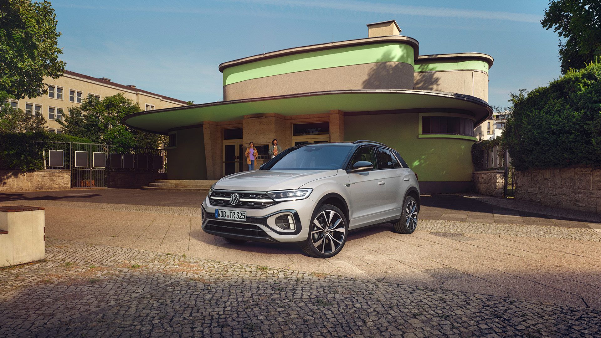 VW T-Roc R-Line in weiß vor einem Gebäude, Front und Seite sichtbar