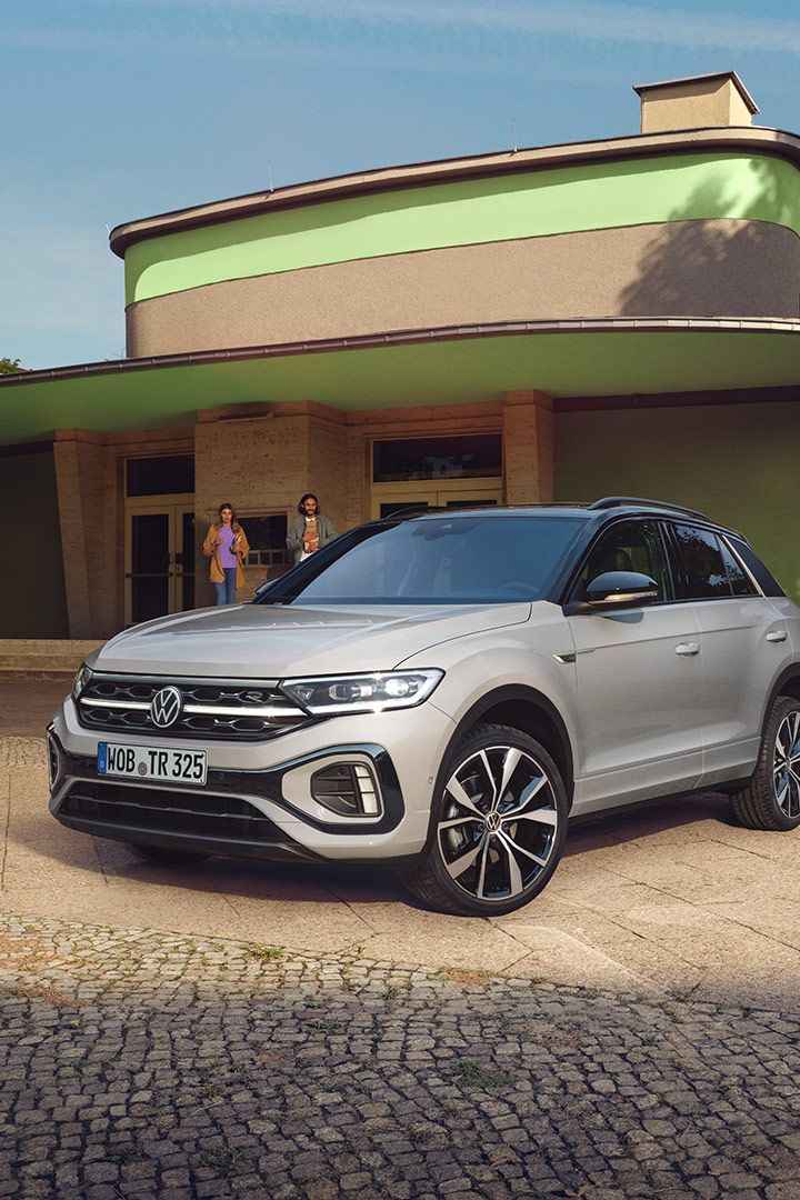 VW T-Roc R-Line in weiß vor einem Gebäude, Front und Seite sichtbar