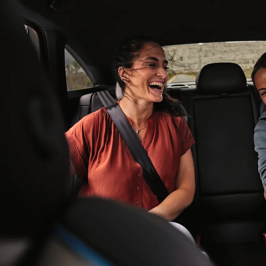Zwei Frauen sitzen auf Rückbank und lachen über Inhalt im Smartphone