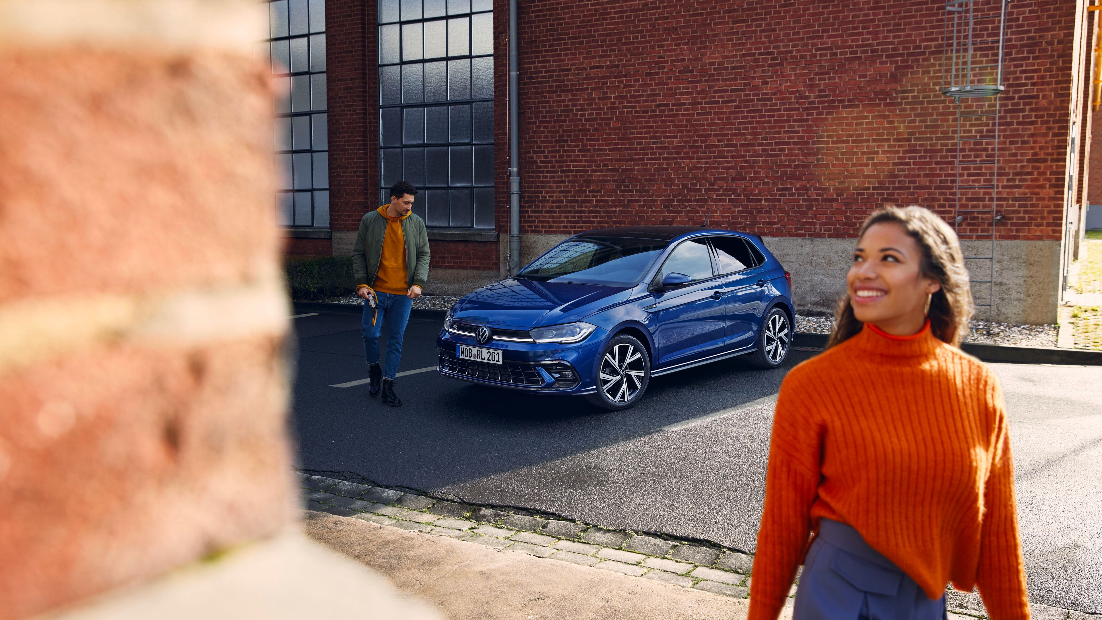 Ein blauer VW Polo steht auf einem Parkplatz, ein Mann steht davor und blickt auf die Motorhaube.