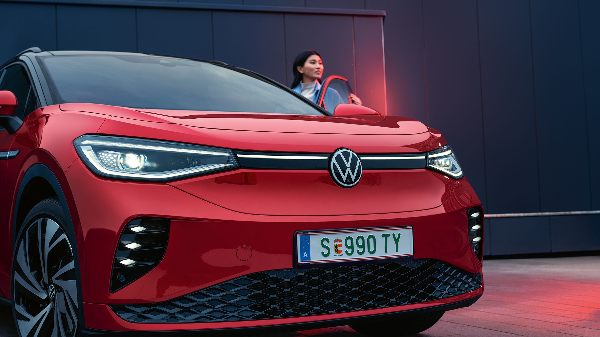 VW ID.4 GTX in rot von hinten beim Laden. Frau steht daneben.