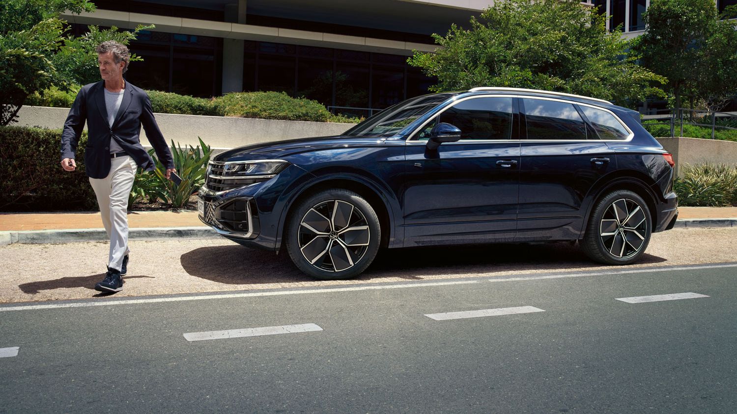 Ein Mann überquert vor einem parkenden VW Touareg R-Line die Straße.