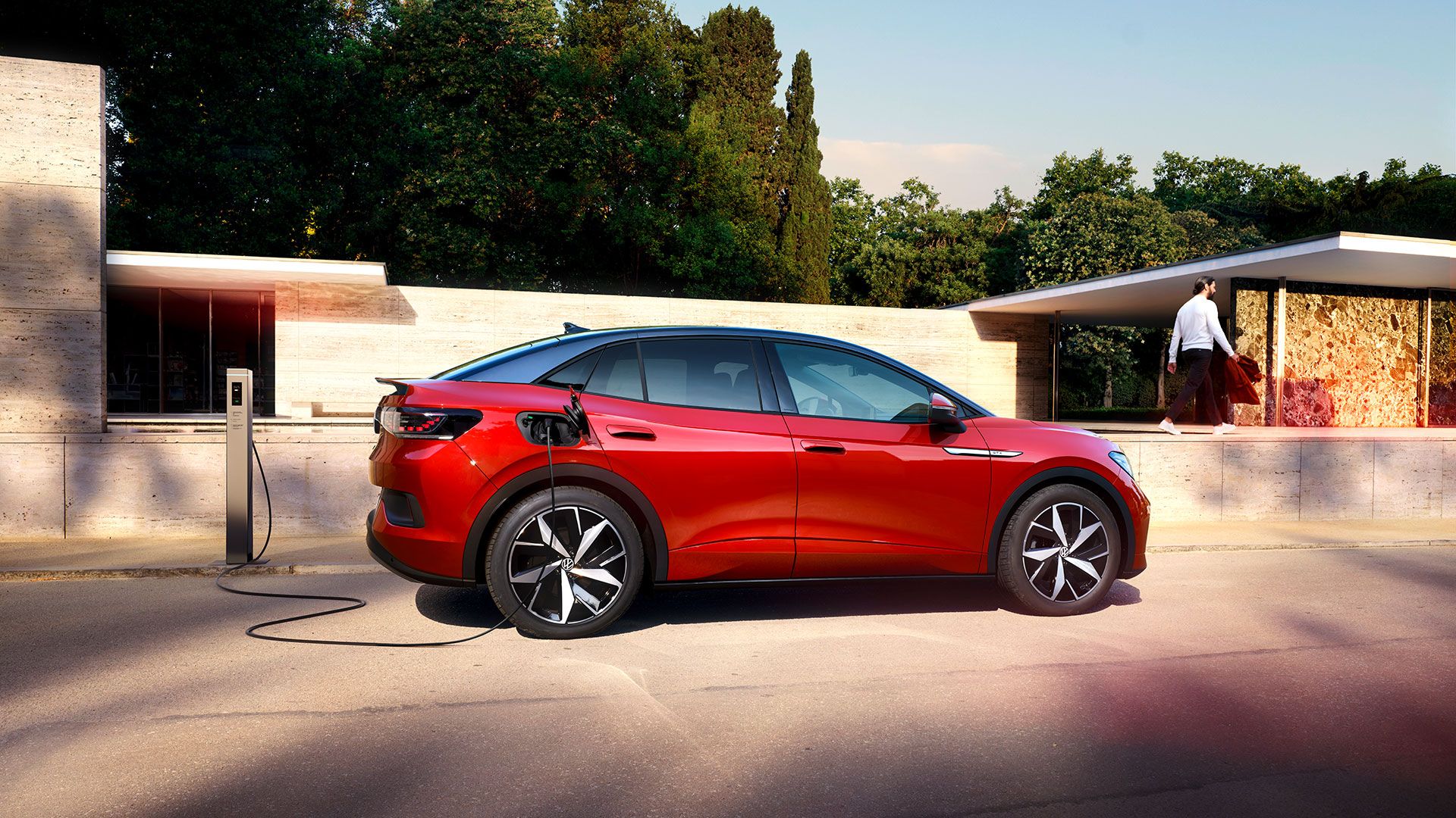Roter VW ID.5 GTX im Exterieur Coupé Design steht vor einem Haus. Per Kabel an eine Ladestation angeschlossen.