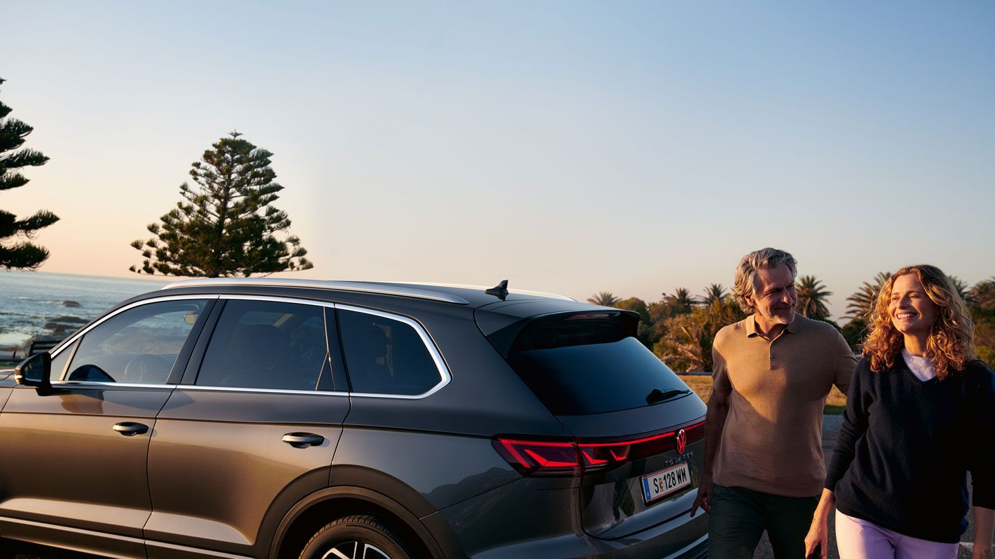 Ein Mann und eine Frau gehen an einem parkenden VW Touareg Elegance vorbei.