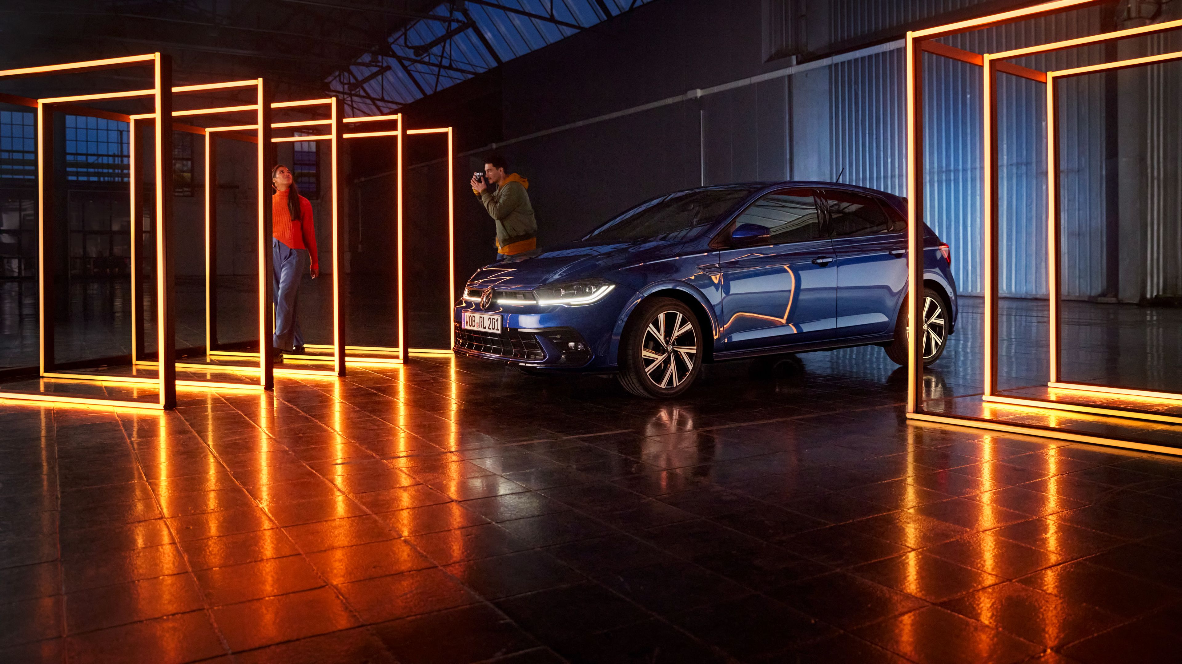 Ein VW Polo in Blau mit LED-Lichtsignatur und LED-Matrix-Scheinwerfern steht in dunkler Halle umgeben von rechteckigen Leuchtelementen.