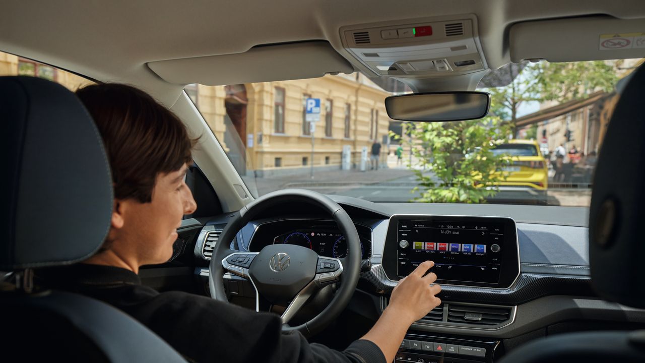 Eine junge Frau bedient vom Fahrersitz aus das Radio über das große Display des Infotainmentsystems.