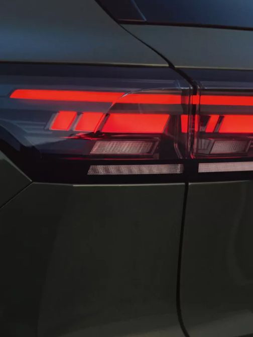 Detailansicht der Heck-Lichtsignatur eines vor einer felsigen Landschaft geparkten dunkelgrünen VW Tiguan.