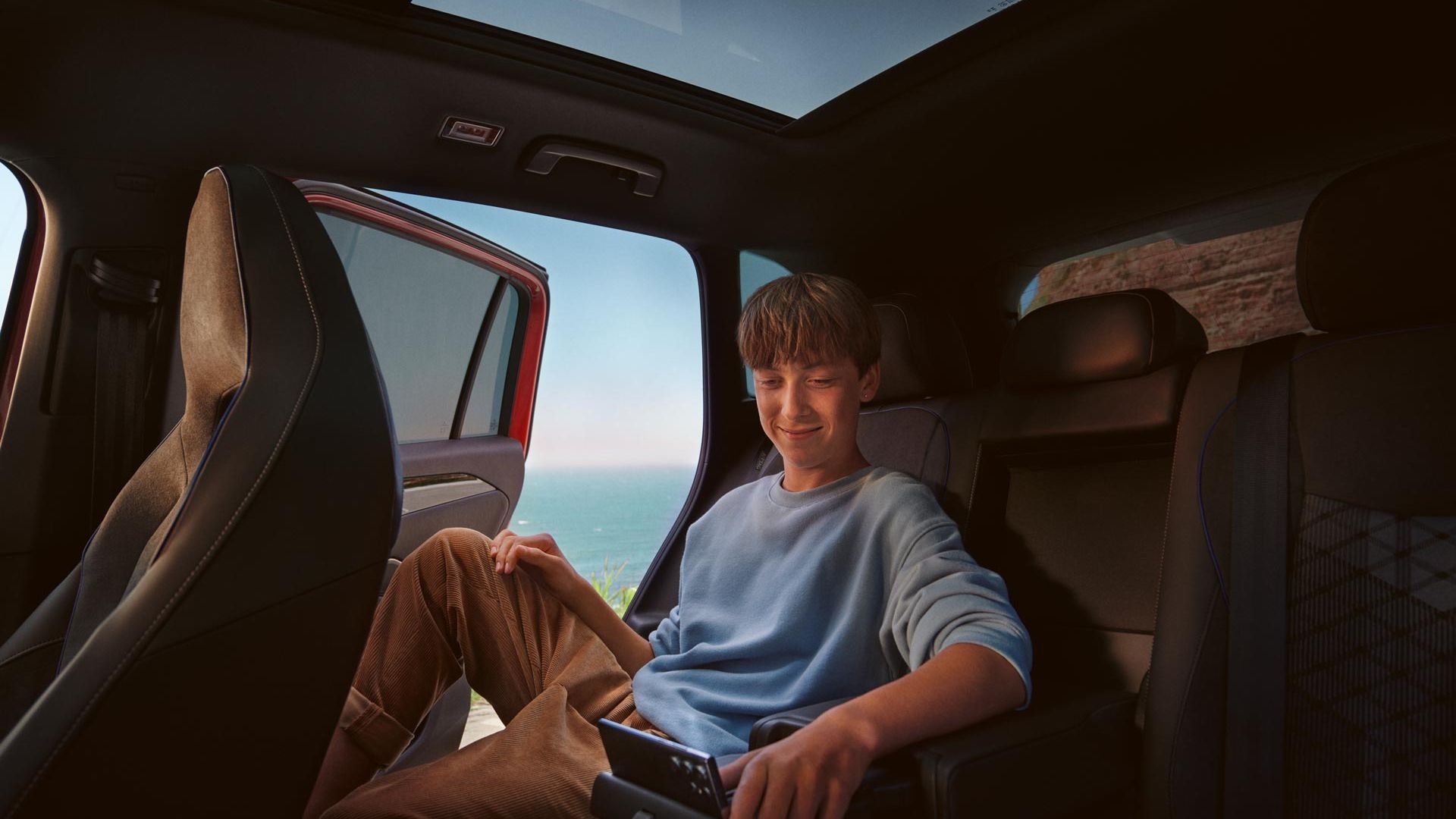 Innenansicht auf die Rückbank des VW Tiguan, wo ein Teenanger auf seinem Tablet, abgestellt auf der Halterung der Mittelkonsole, navigiert. 