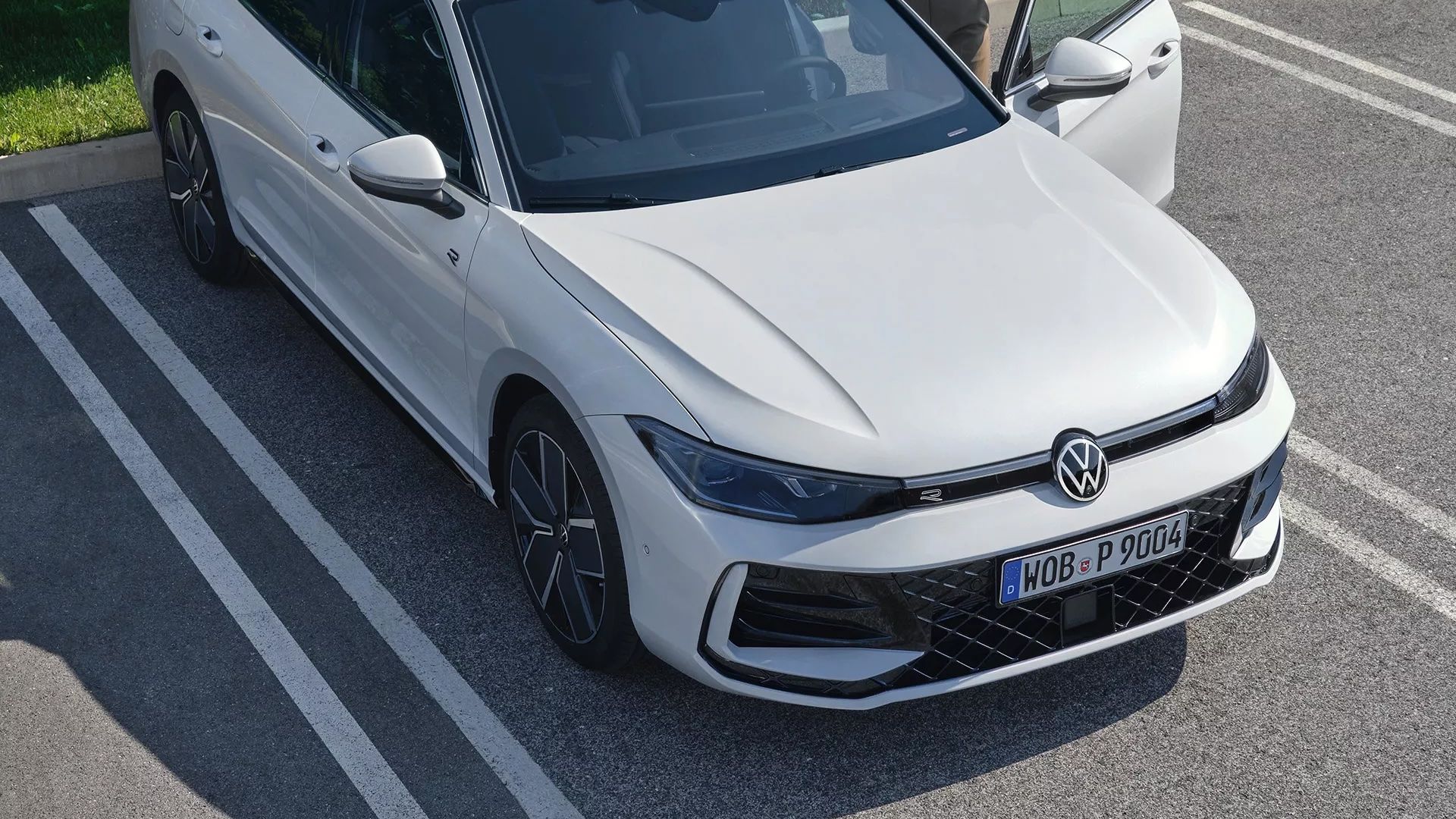 Topshot eines neuen weißen VW Passat auf einem Parkplatz, eine Frau steigt auf der Fahrerseite ein.