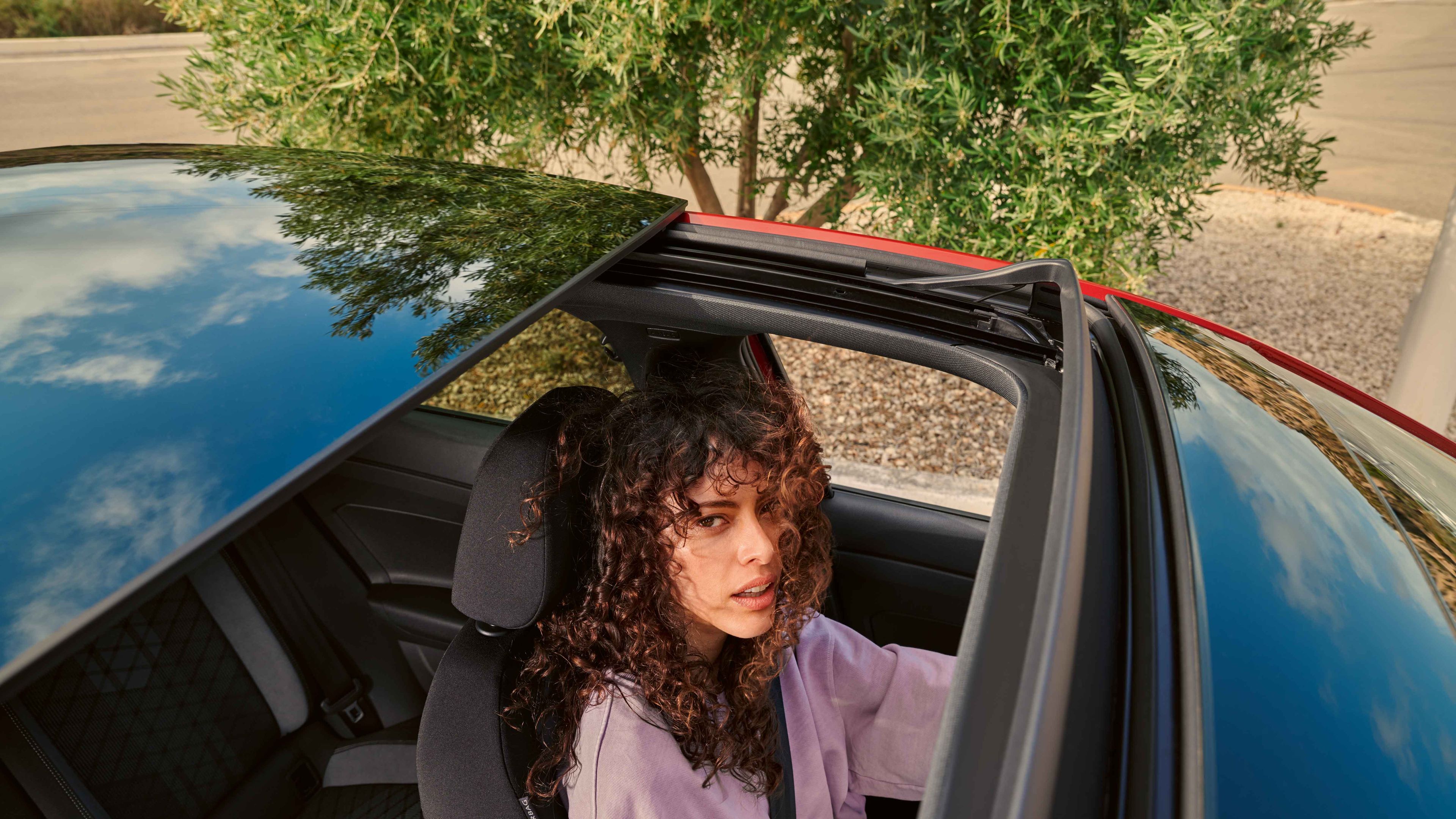 VW Taigo: Blick durchs optionale Panorama-Ausstell/-Schiebedach auf Frau im Fahrersitz