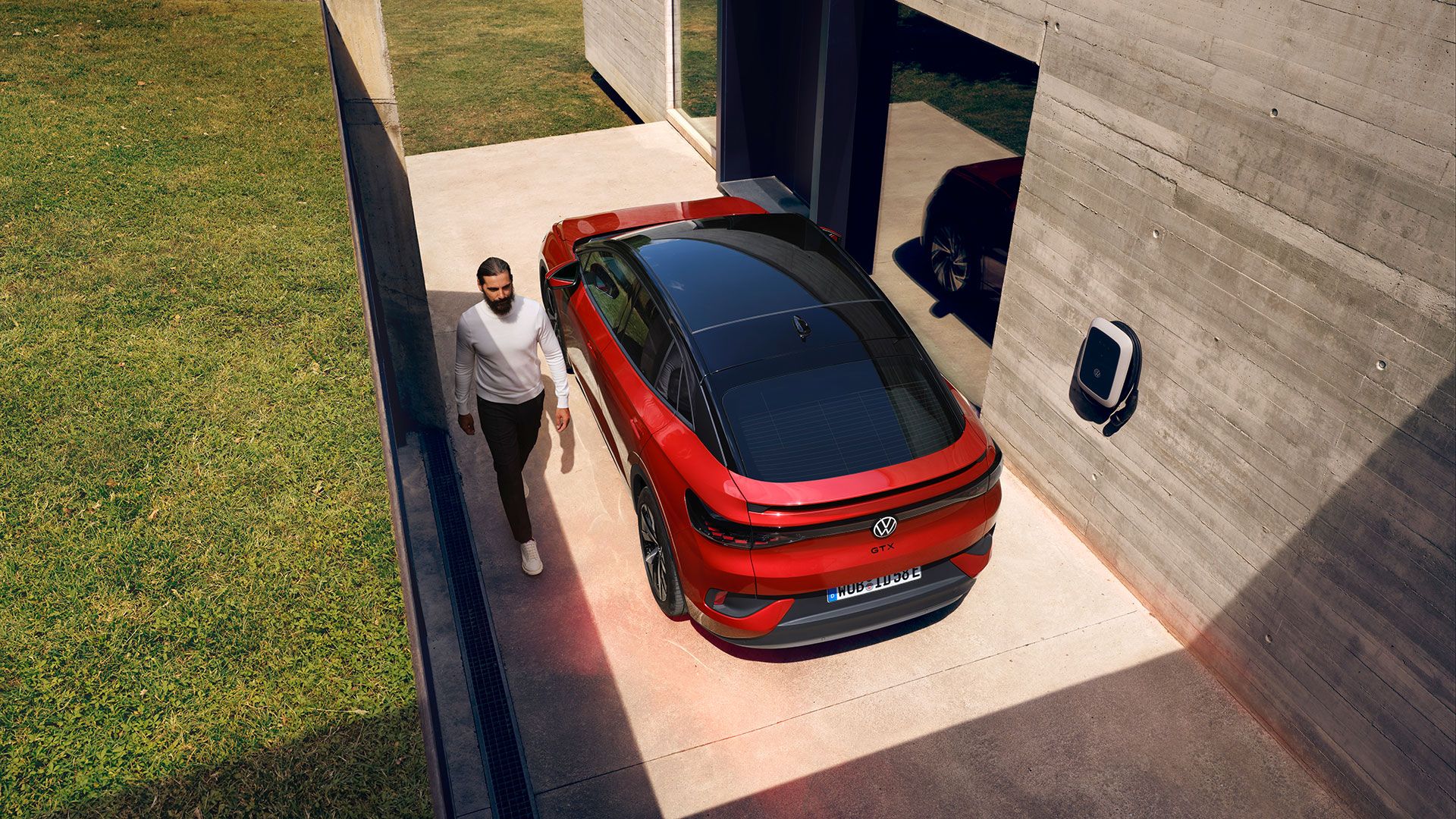 Ein roter VW ID.5 GTX steht neben einem Haus. Blick auf Heck. Ein Mann geht am Fahrzeug vorbei.
