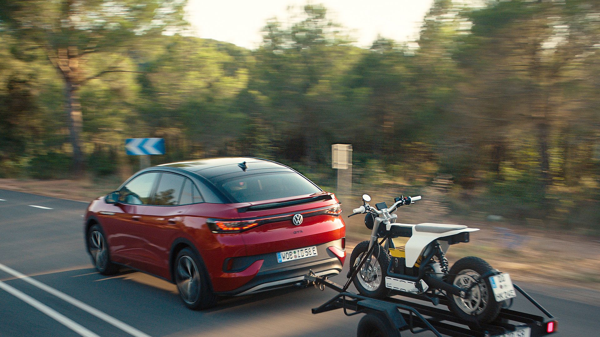 Ein roter VW ID.5 GTX fährt dynamisch auf einer Straße und zieht Anhänger mit Cross-Motorrad.