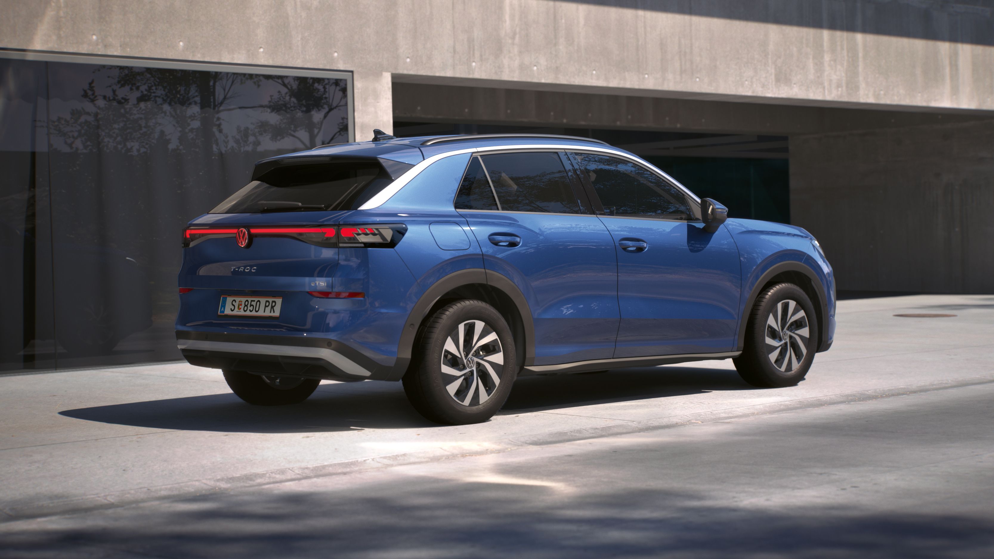 Eine 3/4-Rückansicht eines blauen Volkswagen T-Roc Life, parkend vor einem Gebäude.
