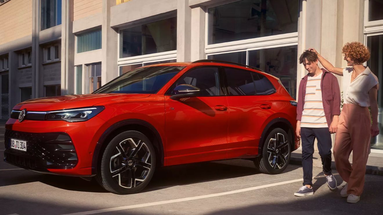 Roter VW Tiguan parkt vor einem Gebäude, daneben gehen eine Frau und ein Jugendlicher.