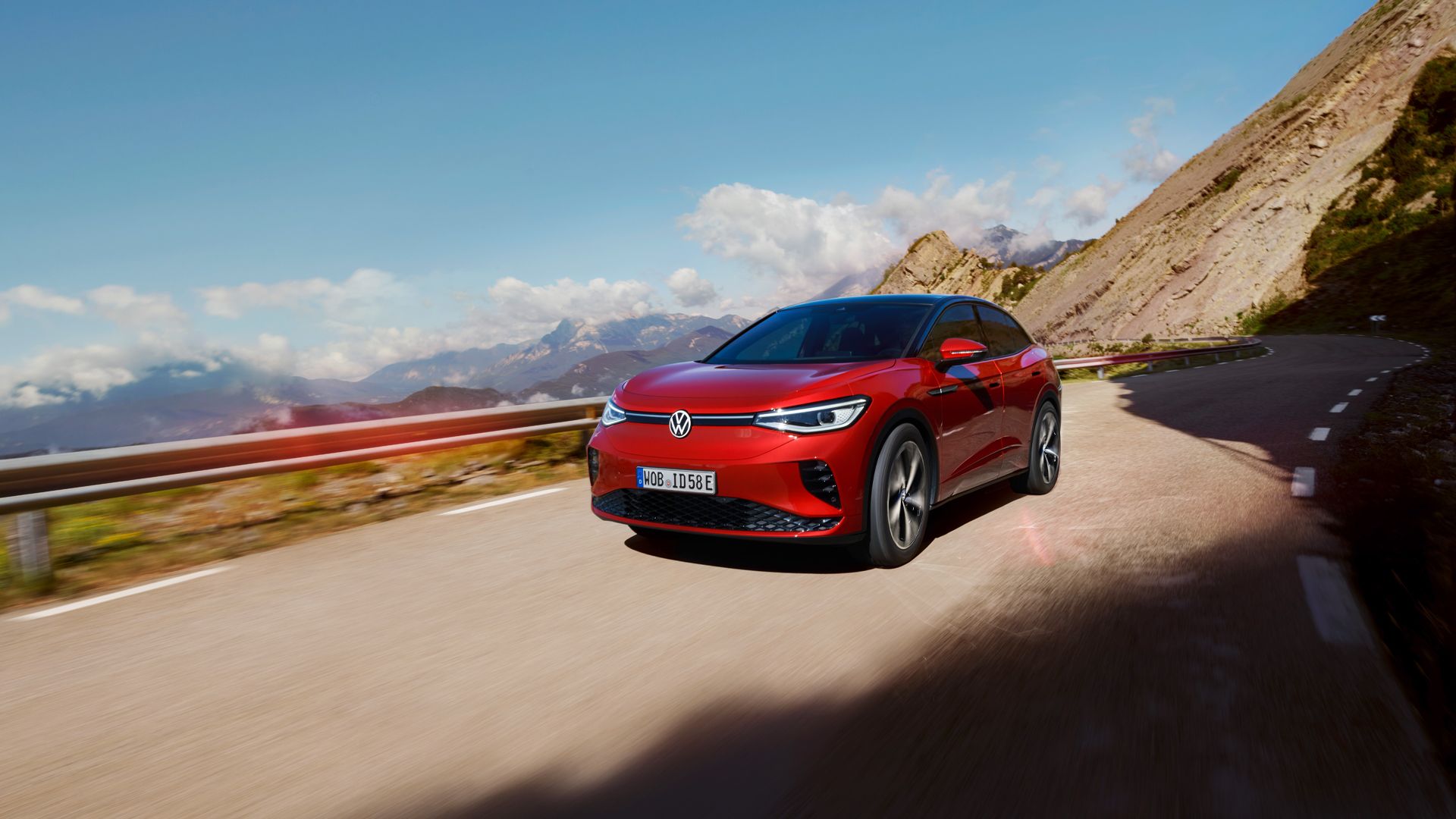Roter VW ID.5 GTX fährt dynamisch auf einer Bergstraße. Blick auf Front, Räder und Seite.