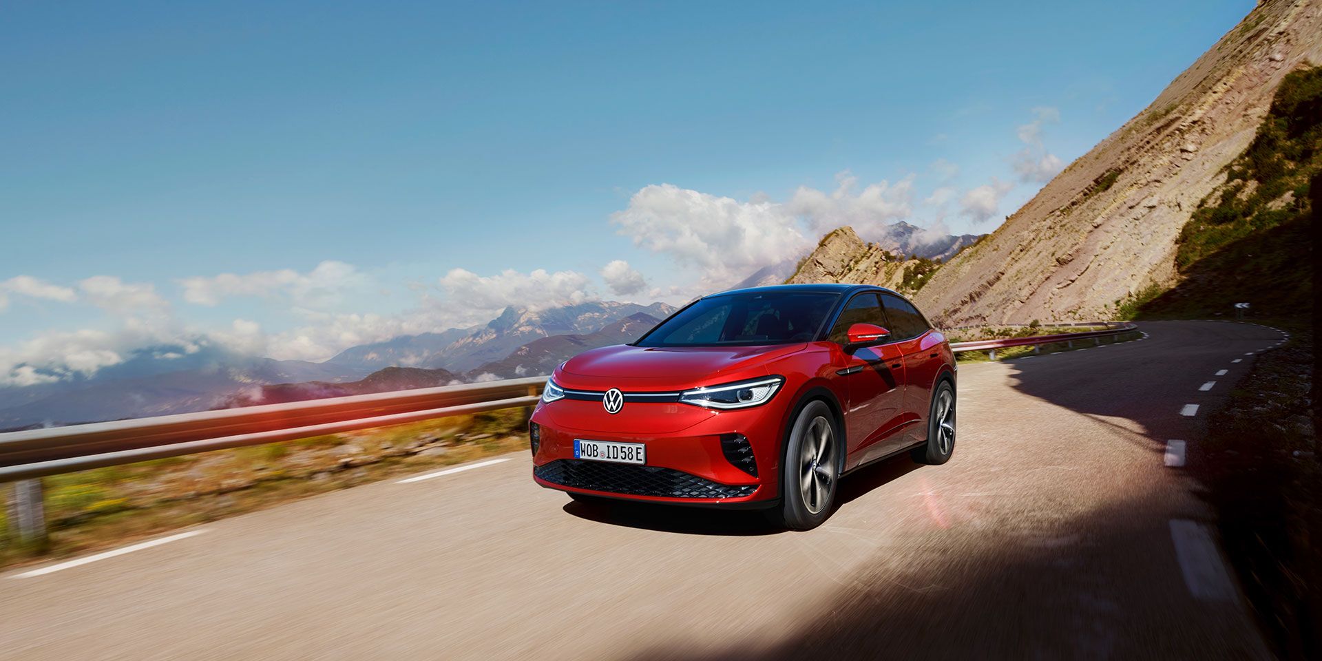Roter VW ID.5 GTX fährt dynamisch auf einer Bergstraße. Blick auf Front, Räder und Seite.