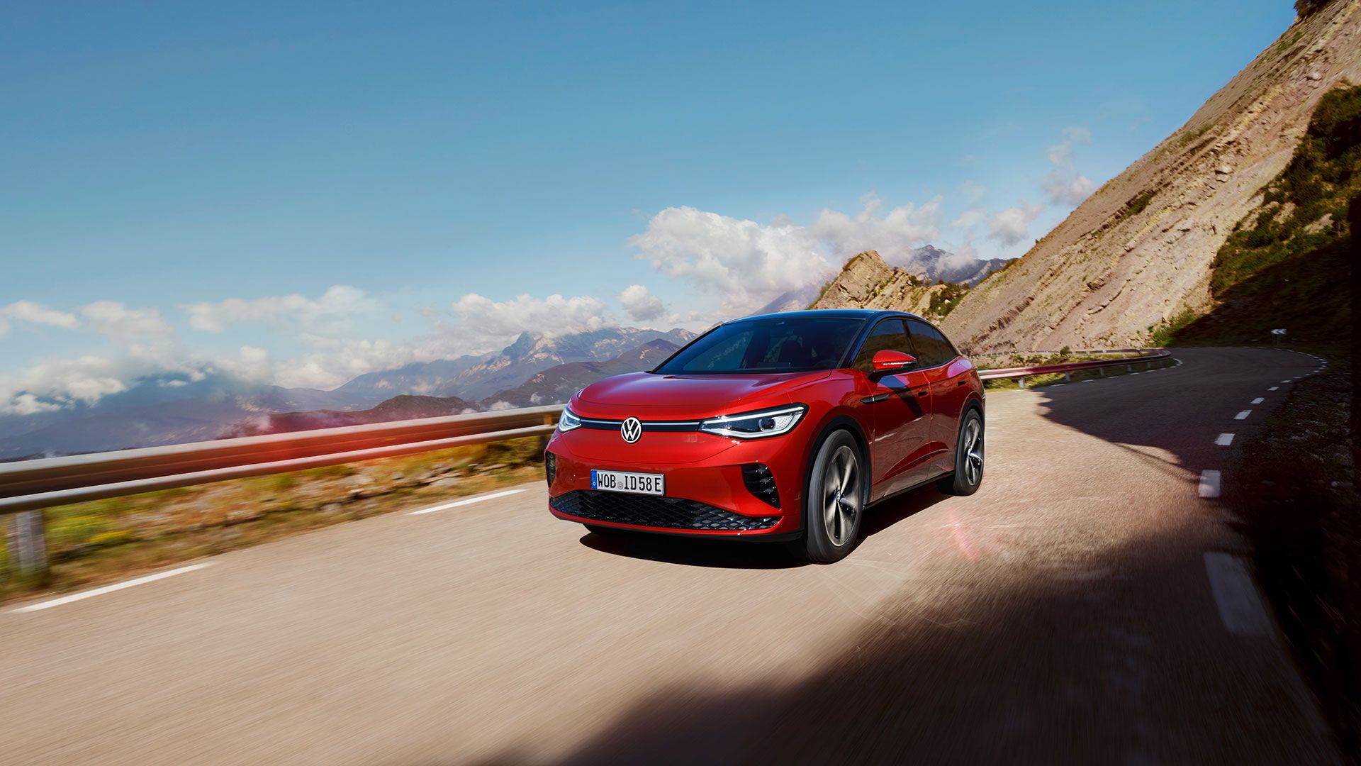 Roter VW ID.5 GTX fährt dynamisch auf einer Bergstraße. Blick auf Front, Räder und Seite.