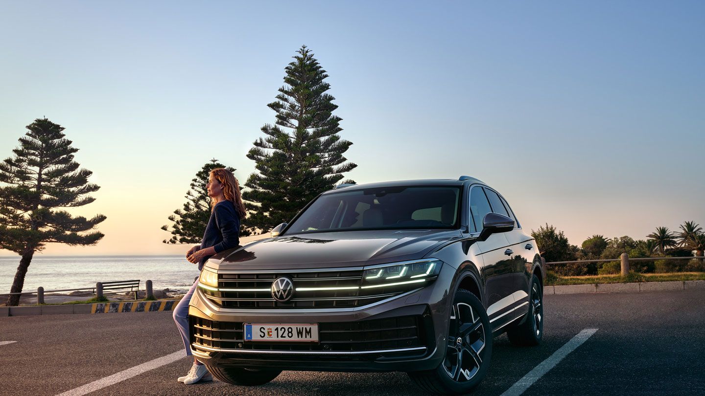 Ein VW Touareg Elegance in der Dämmerung am Meer mit eingeschalteten HD-Matrix-Scheinwerfern. 