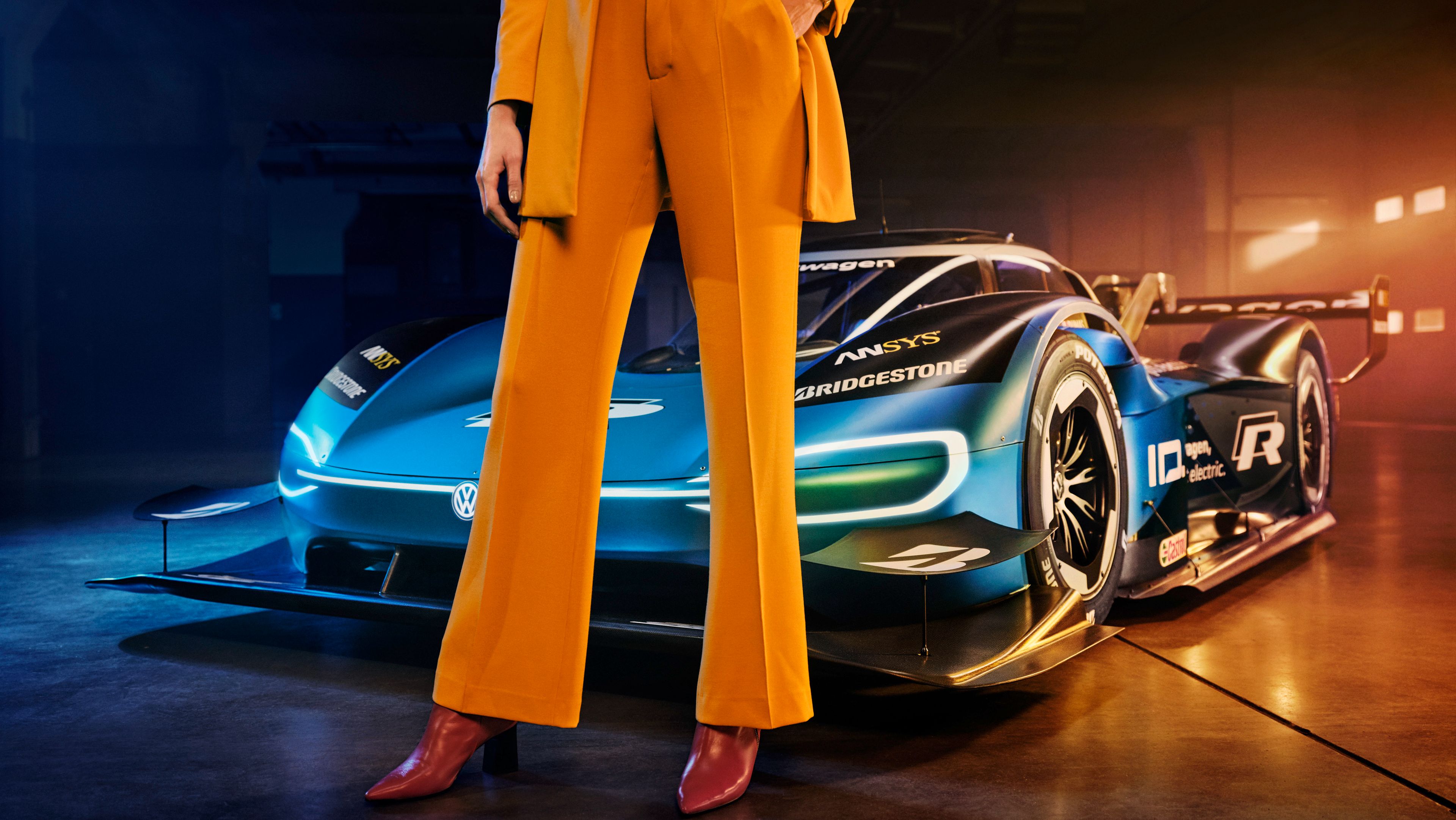 weibliches Model in Hosenanzug vor dem Volkswagen ID.R, elektrisch angetriebener Rennwagen, Lagerhalle