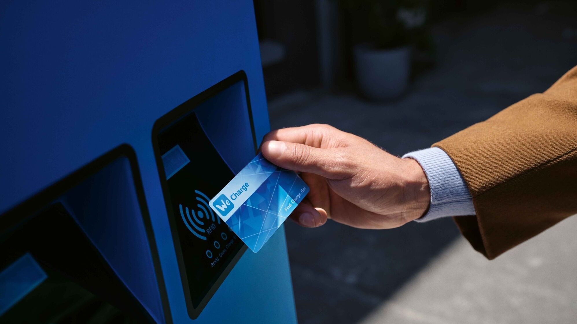 Mann hält We Charge Ladekarte an blaues Bezahlterminal.