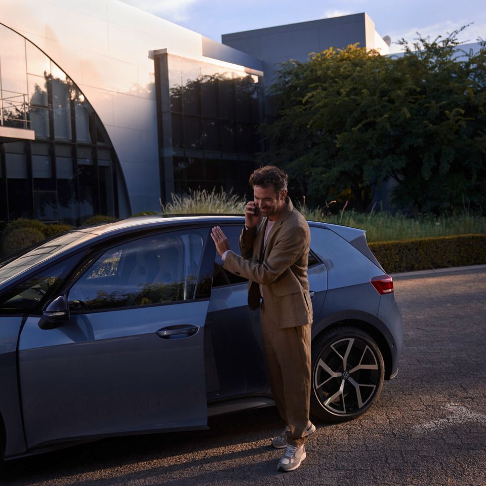 Ein Mann steht vor einem blauen VW ID.3 Neo und telefoniert per Smartphone