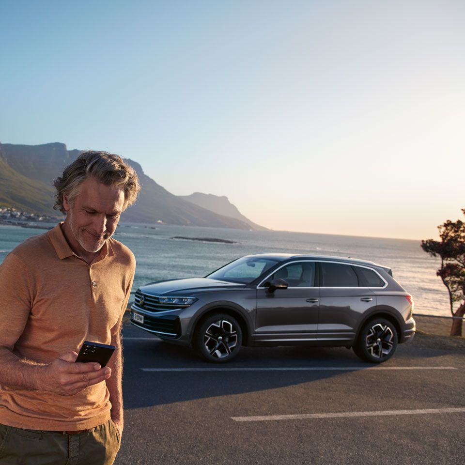 Mann lehnt an VW T-Cross mit Smartphone in der Hand und liest Newsletter