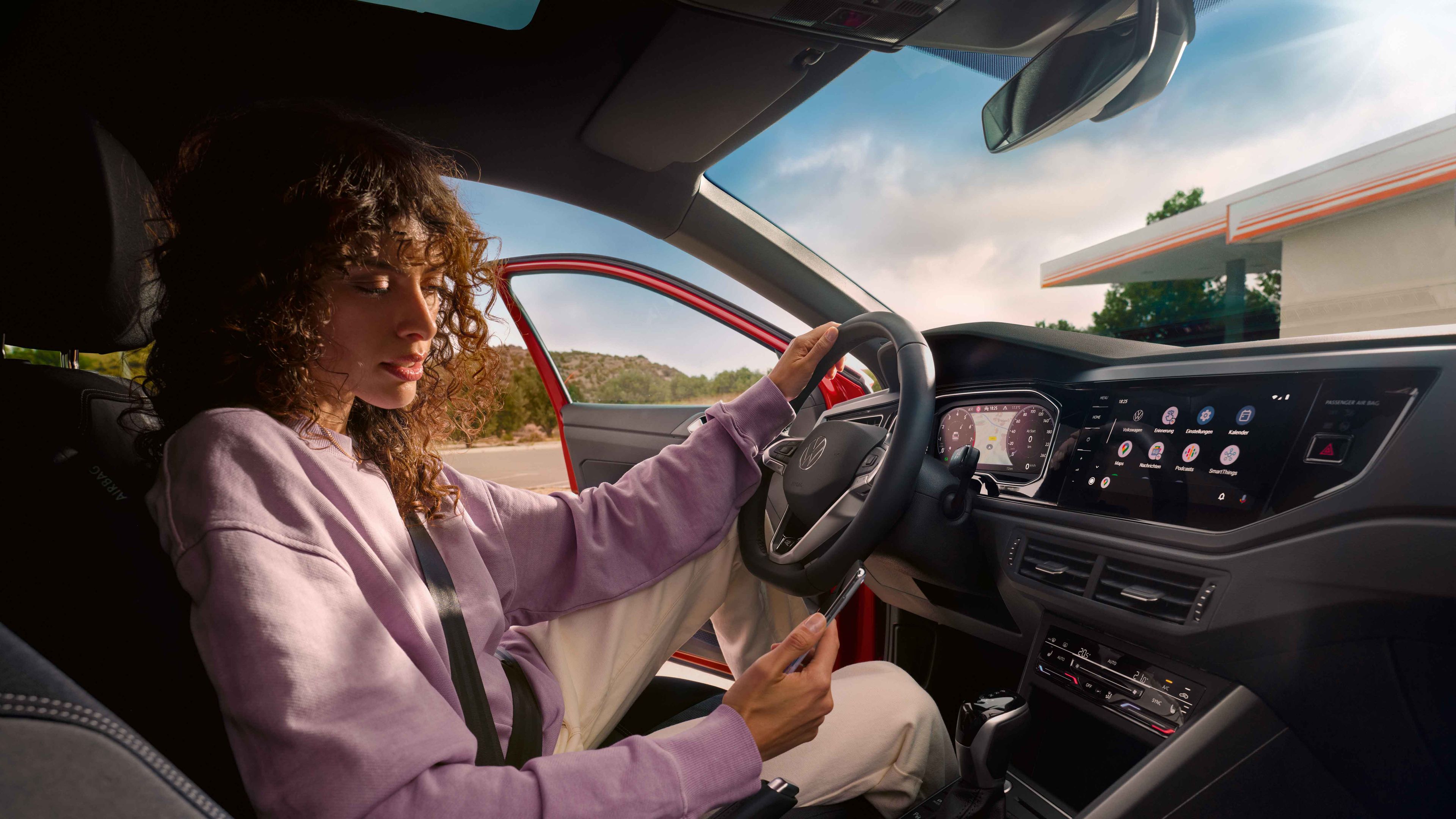 VW Taigo Interieur: Frau sitzt auf Fahrersitz in parkendem Auto und schaut aufs Smartphone