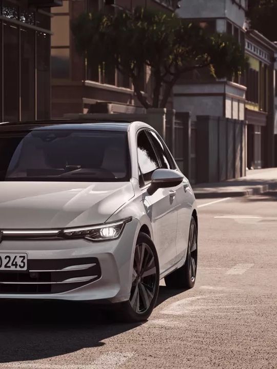 Weißer VW Golf fährt auf einer Straße auf eine Kreuzung zu.