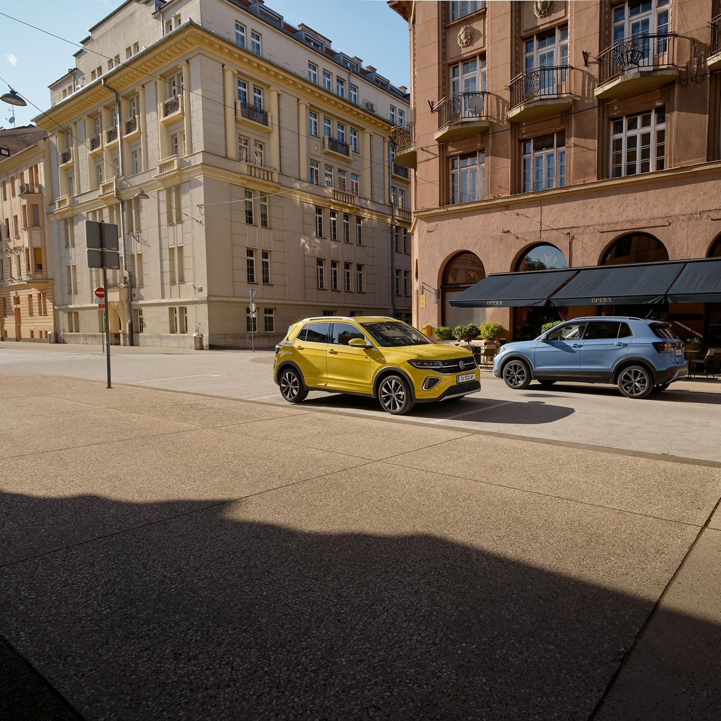 Ein gelber und ein blauer VW T-Cross fahren auf einer Straße aneinander vorbei.