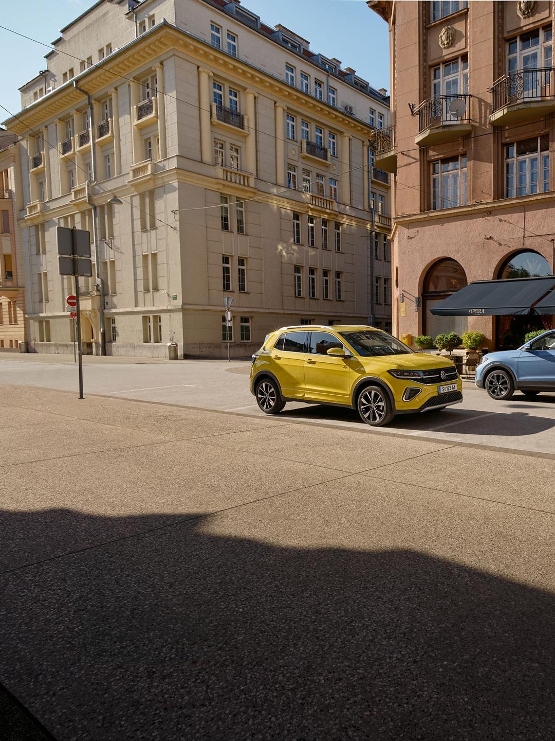 Ein gelber und ein blauer VW T-Cross fahren auf einer Straße aneinander vorbei.