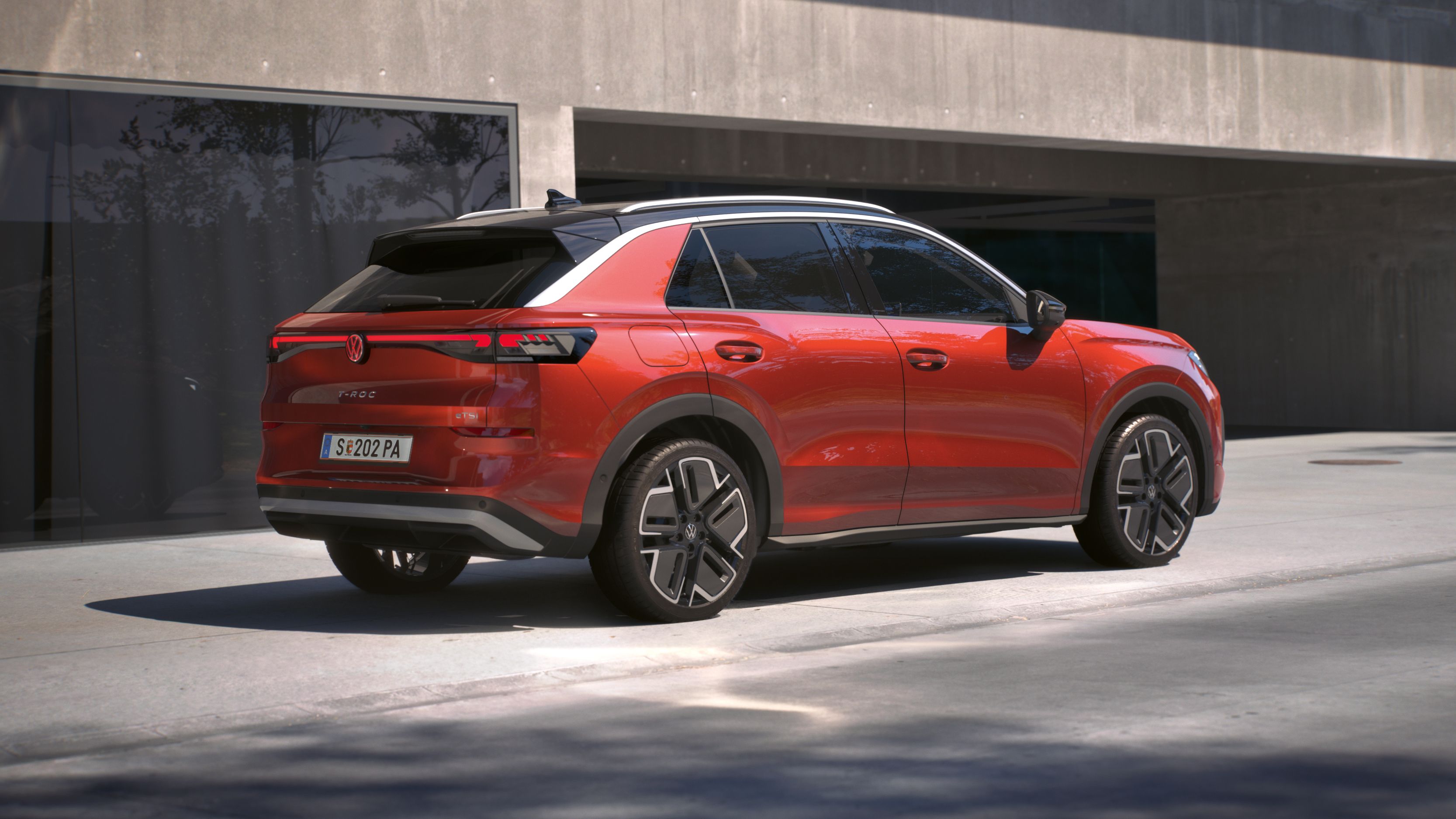 Eine 3/4-Rückansicht eines roten Volkswagen T-Roc Style, parkend vor einem Gebäude.