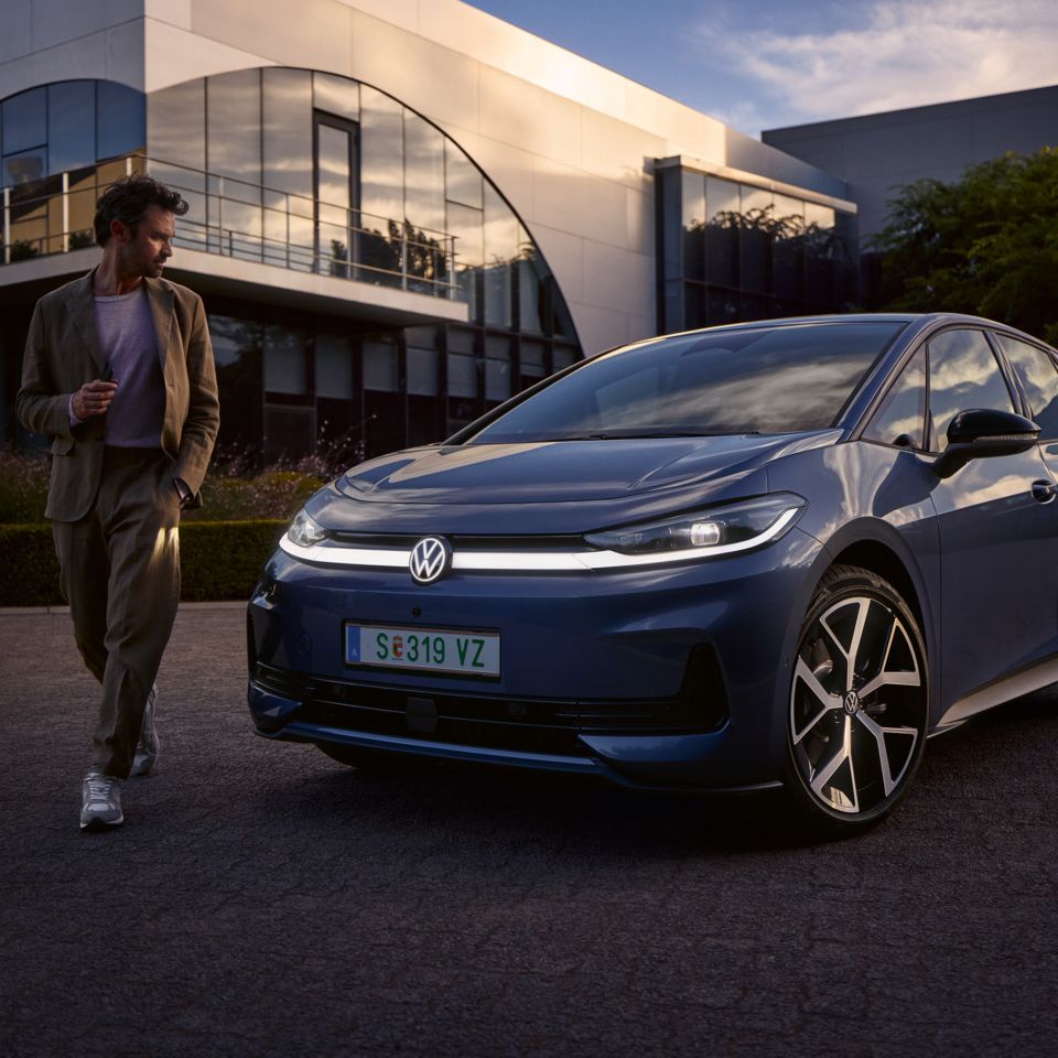 Ein Mann geht um die Front eines blauen VW ID.3 Neo und betrachtet das Lichtdesign