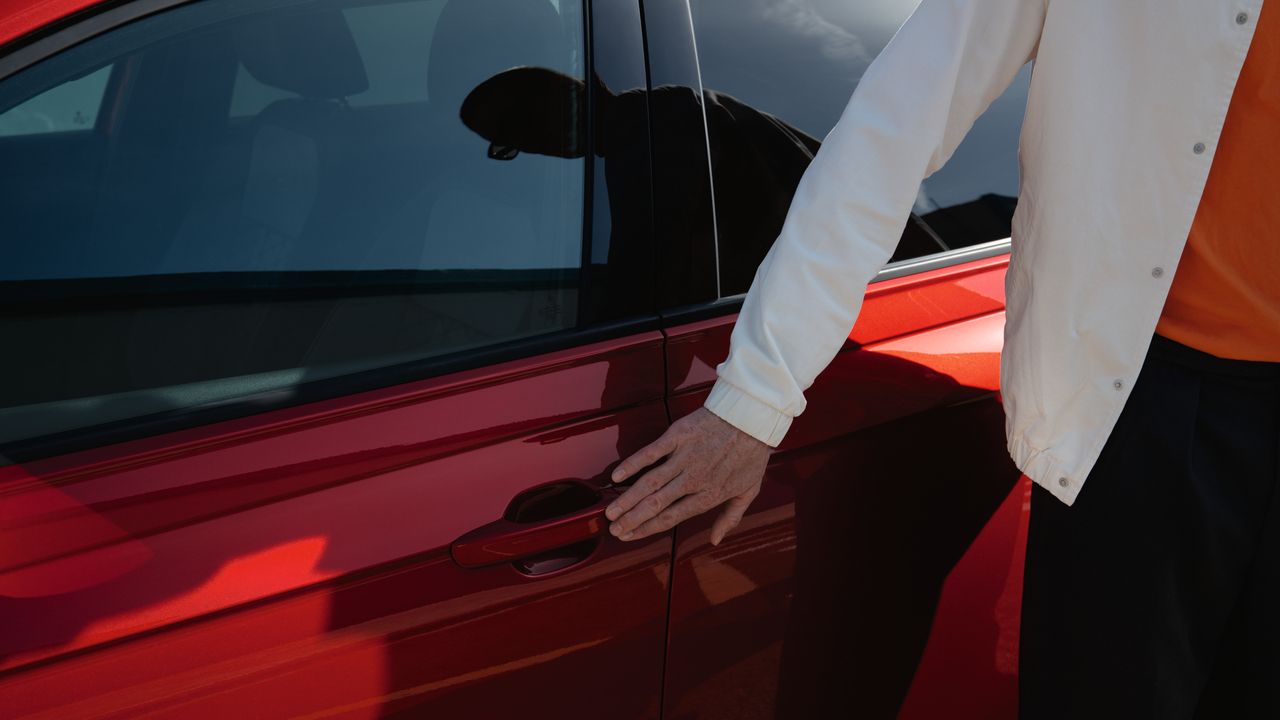 Mann streift mit Hand den Türgriff eines roten VW Taigo