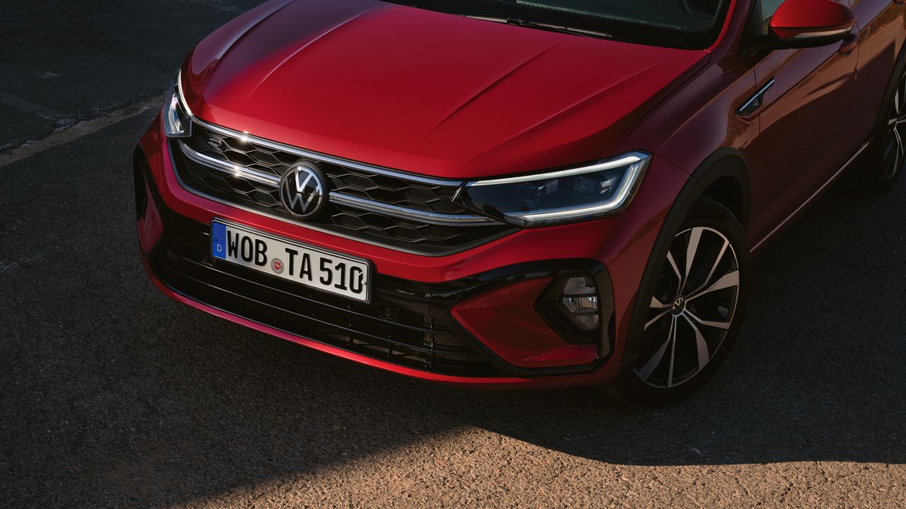 VW Taigo R-Line Front in Rot auf Parkplatz. Licht eingeschaltet. Frau lehnt an Motorhaube.