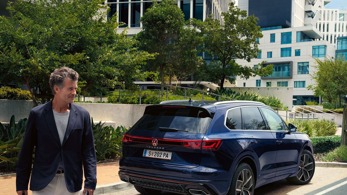 Ein Mann überquert die Straße, schräg hinter ihm ein am Straßenrand parkender VW Touareg R-Line.