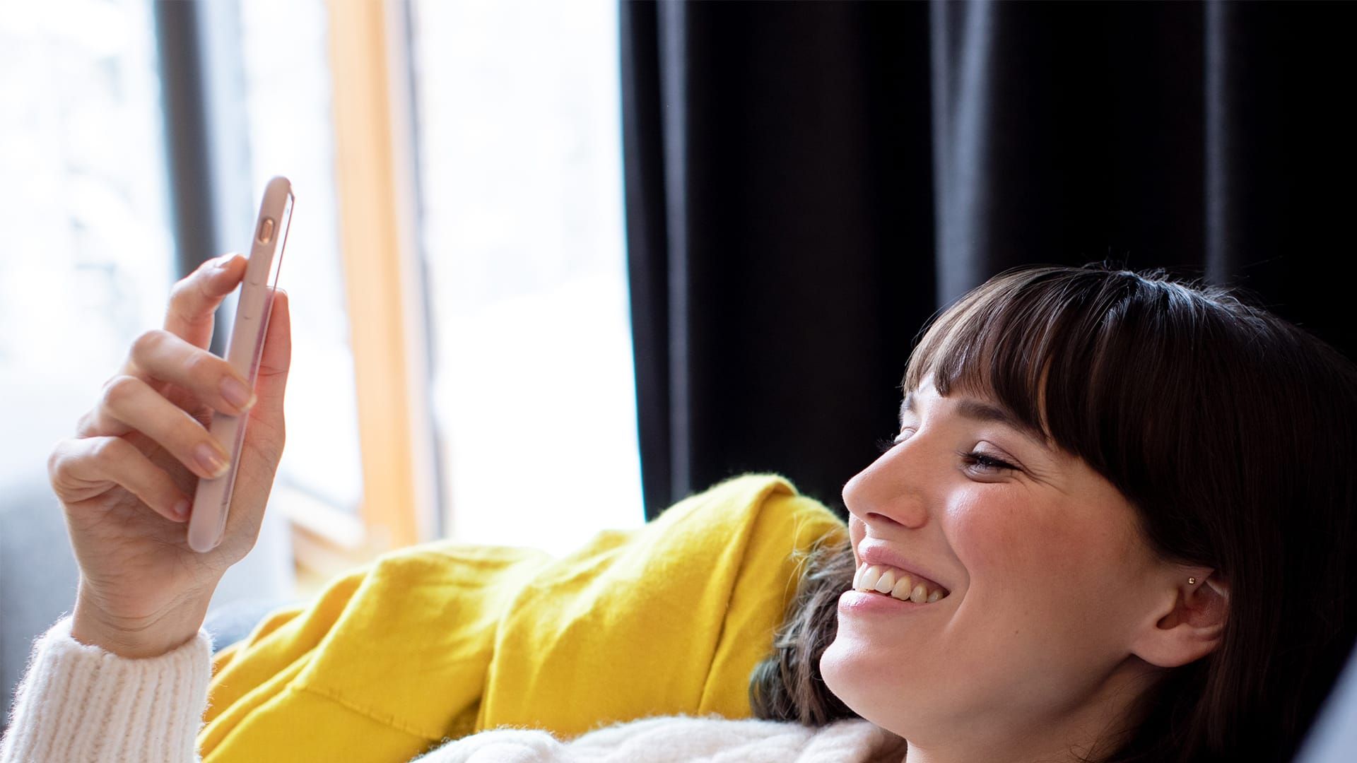 Liegende Frau blickt lächelnd auf ein Smartphone