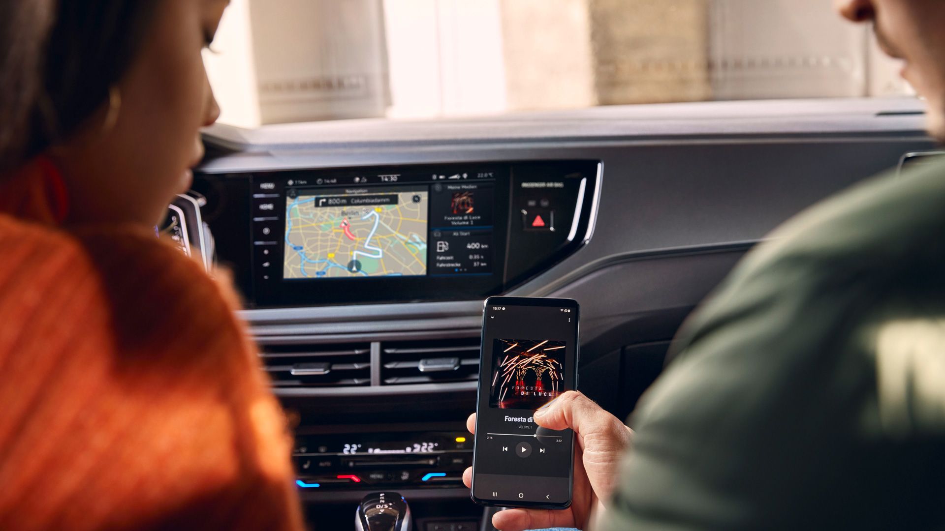 Zwei Personen sitzen vorne im VW Polo, von rechts wird ein Smartphone hoch gehalten, das sich kabellos mit dem Infotainment-System verbindet. 