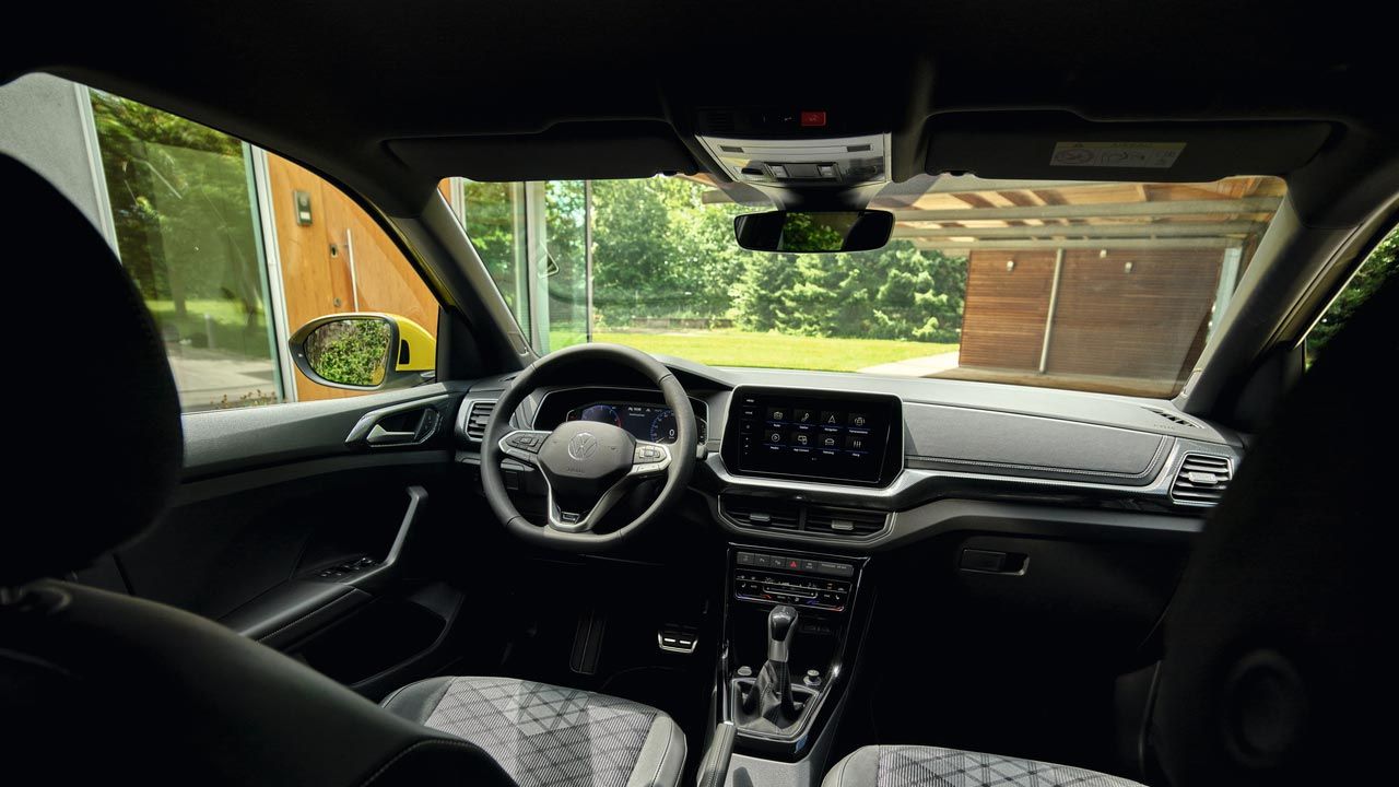 Blick vom Rücksitz aus ins Cockpit und durch die Frontscheibe auf ein Haus mit Garten.