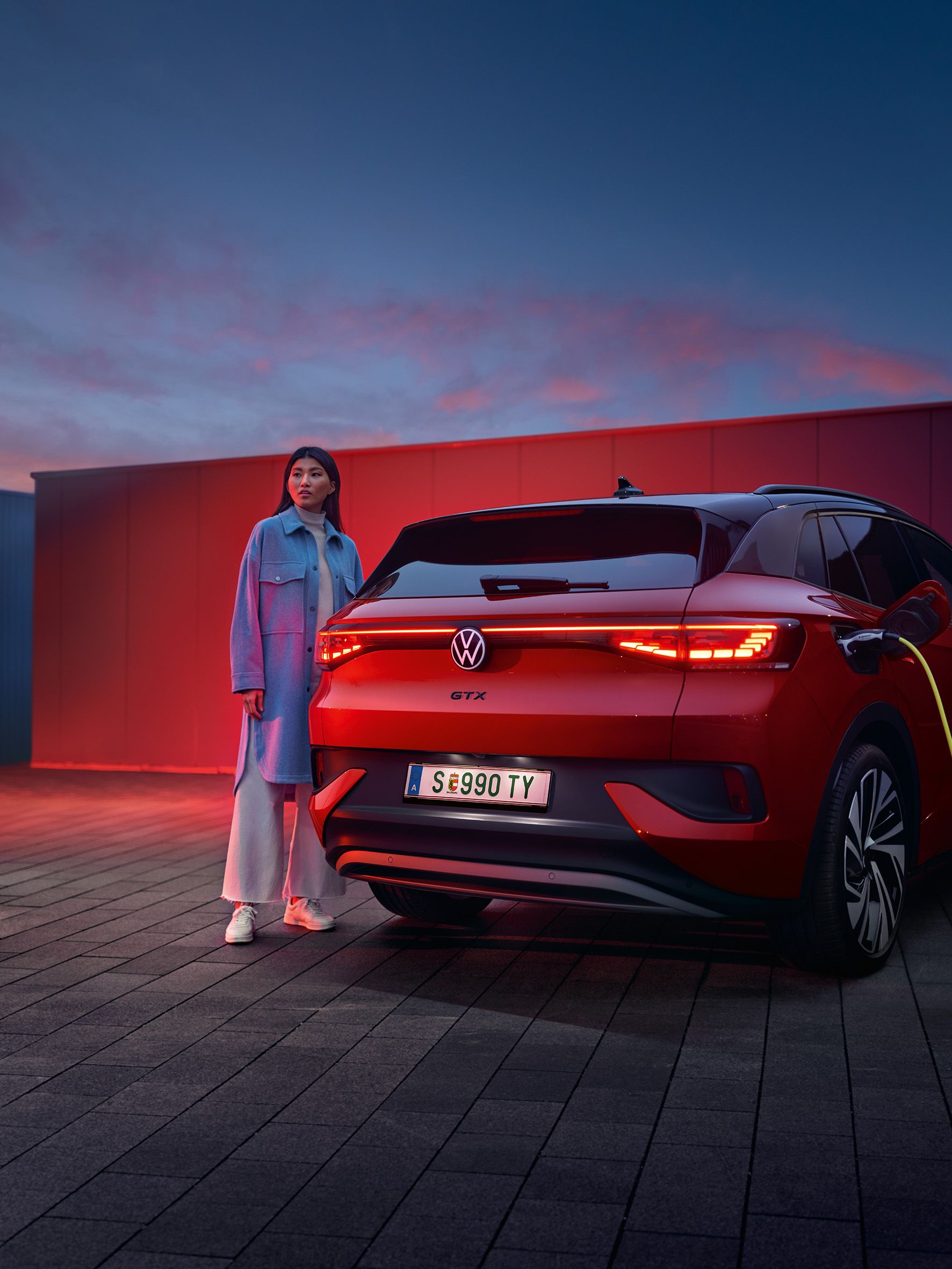 Seitenansicht des VW Tiguan eHybrid in Weiß, welcher am Straßenrand lädt. Junger Mann steigt aus Fahrerseite aus.