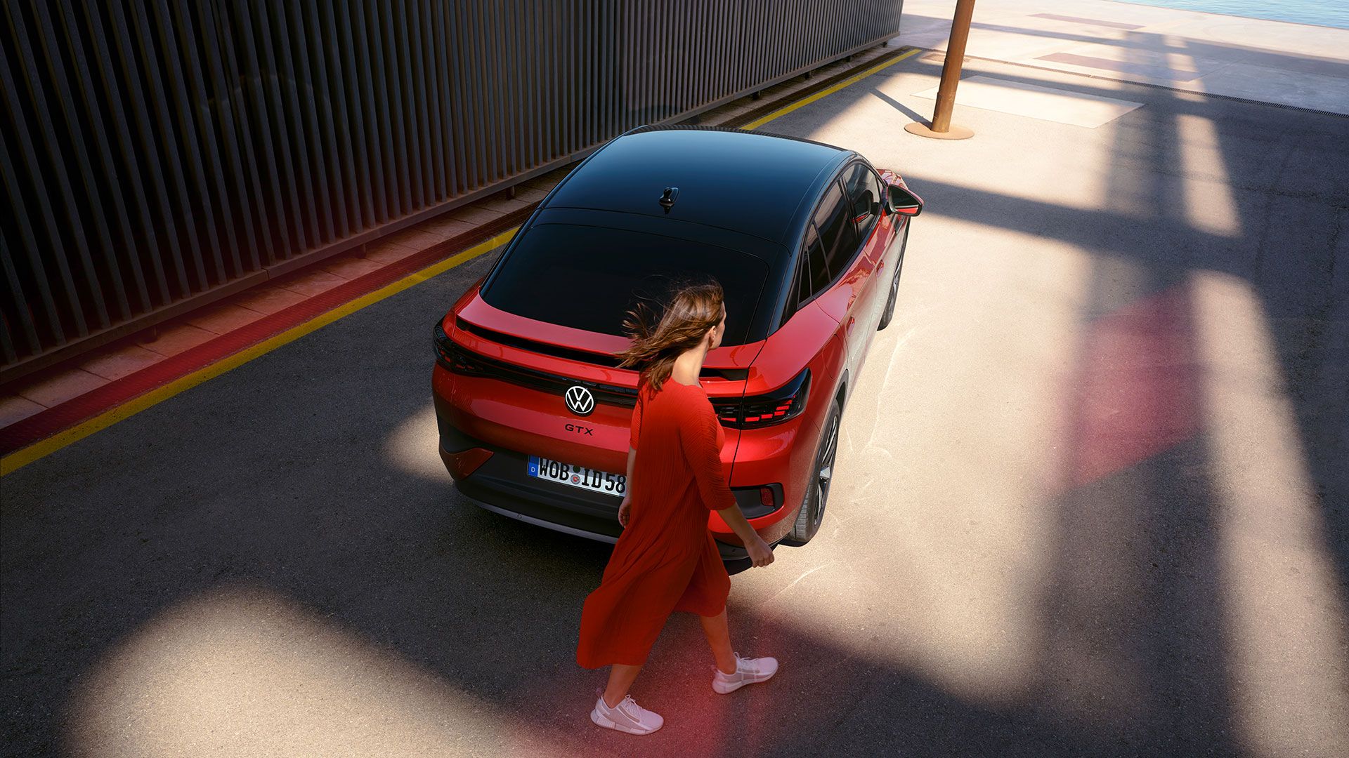 Roter VW ID.5 GTX in einer Seitenstraße. Blick von oben auf Dach und Heck. Eine junge Frau geht vorbei.