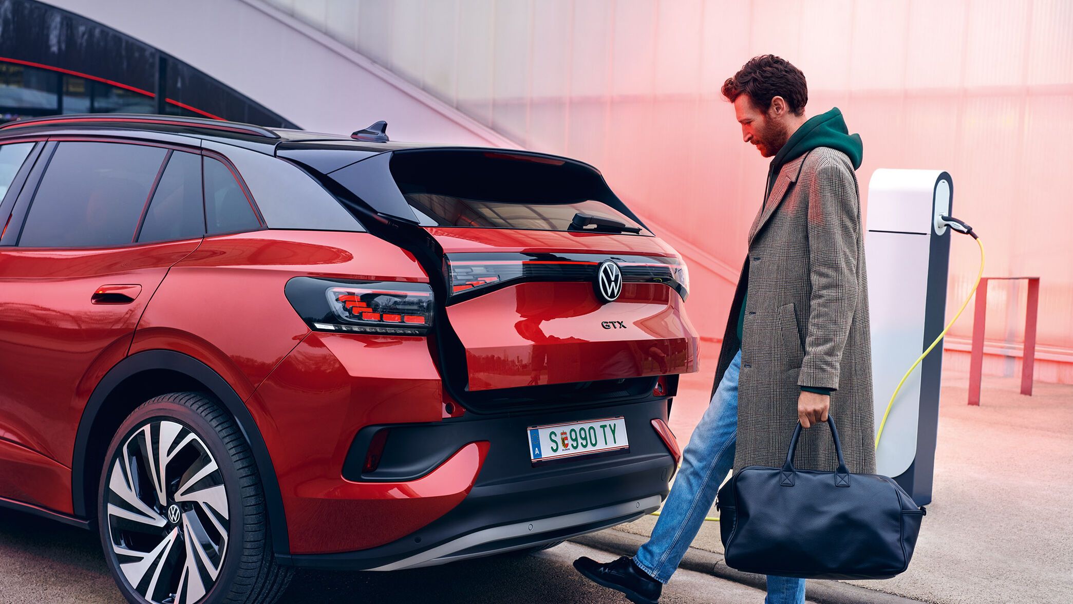 VW ID.4 GTX in Rot von hinten zu sehen, Mann mit Tasche öffnet Heckklappe