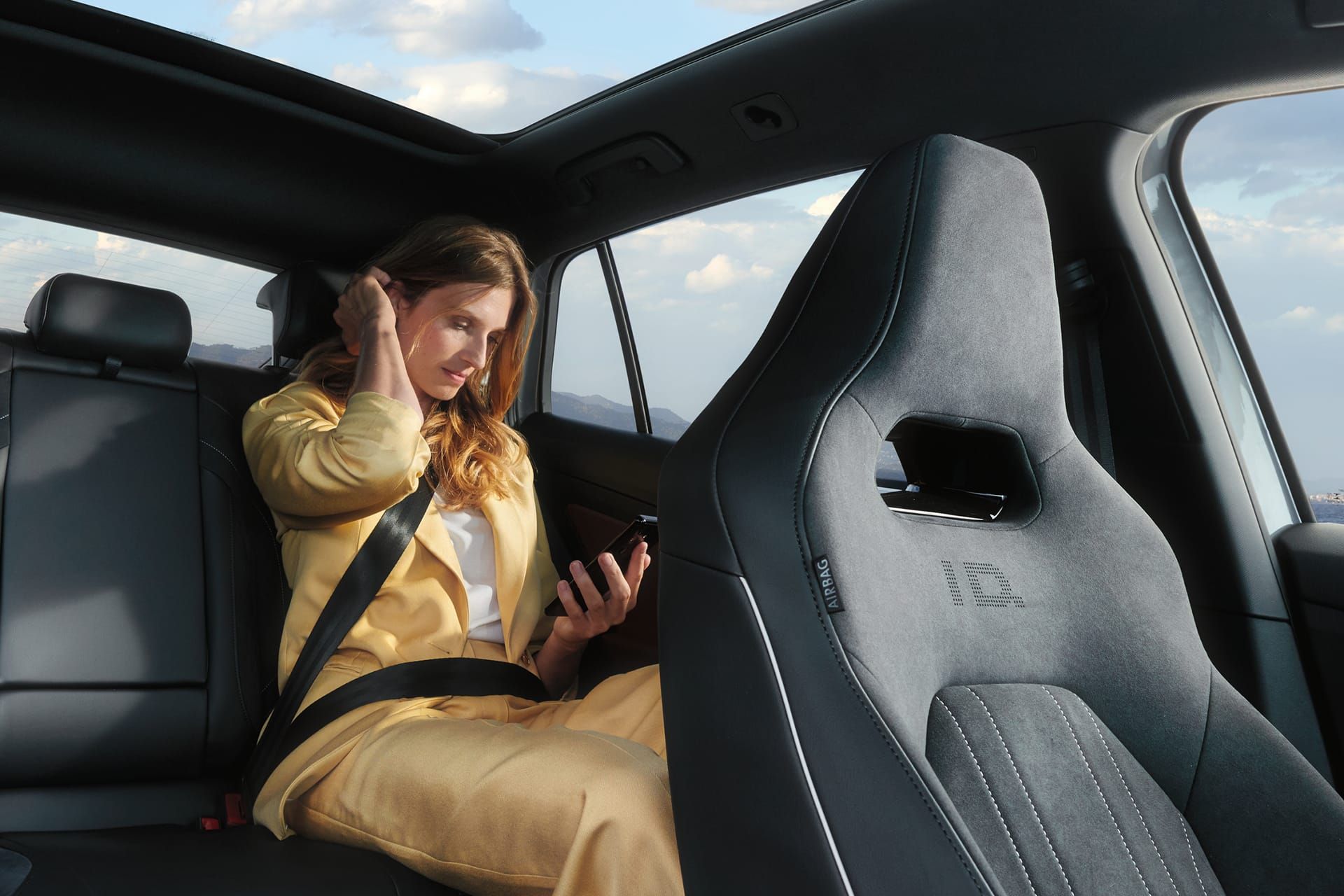 VW ID.5 Interieur, Blick auf die Rücksitzbank, Frau sitzt im Auto und schaut auf ihr Handy.