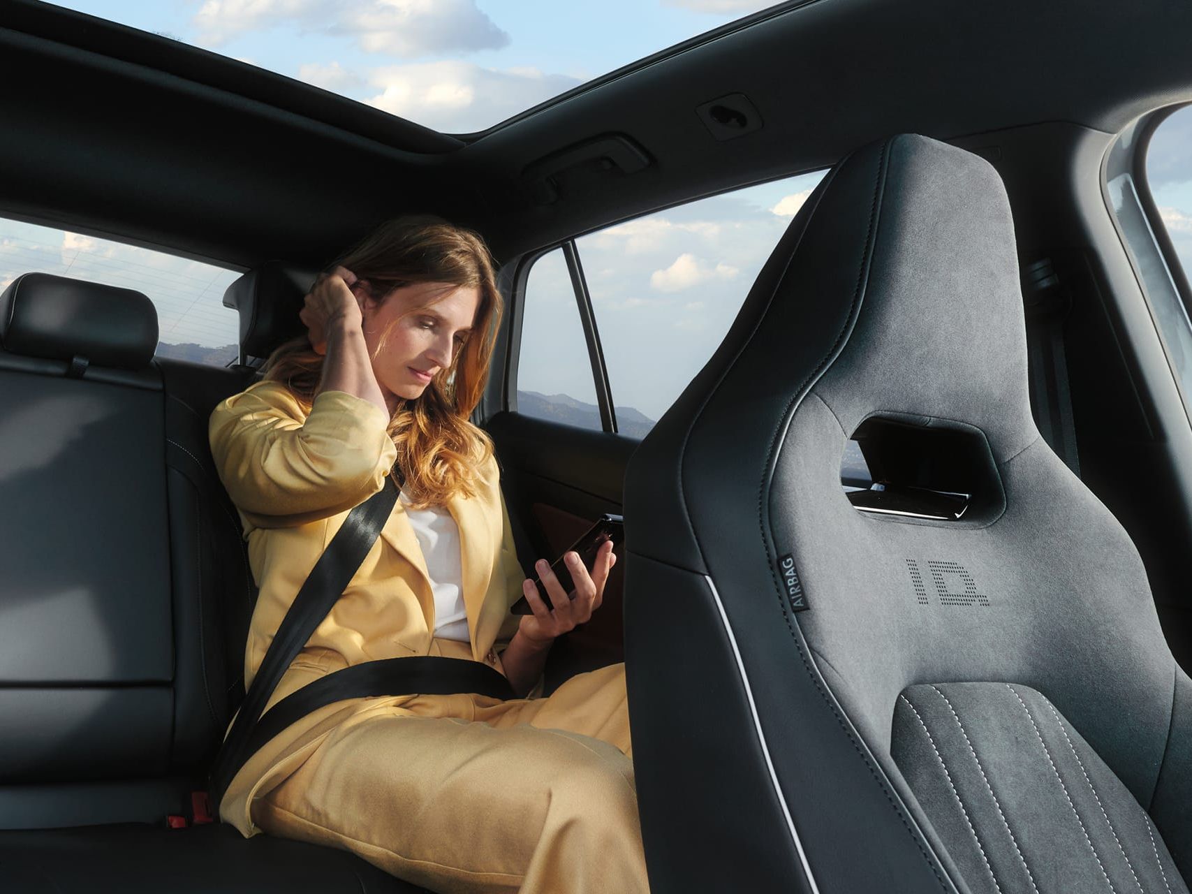 VW ID.5 Interieur, Blick auf die Rücksitzbank, Frau sitzt im Auto und schaut auf ihr Handy.
