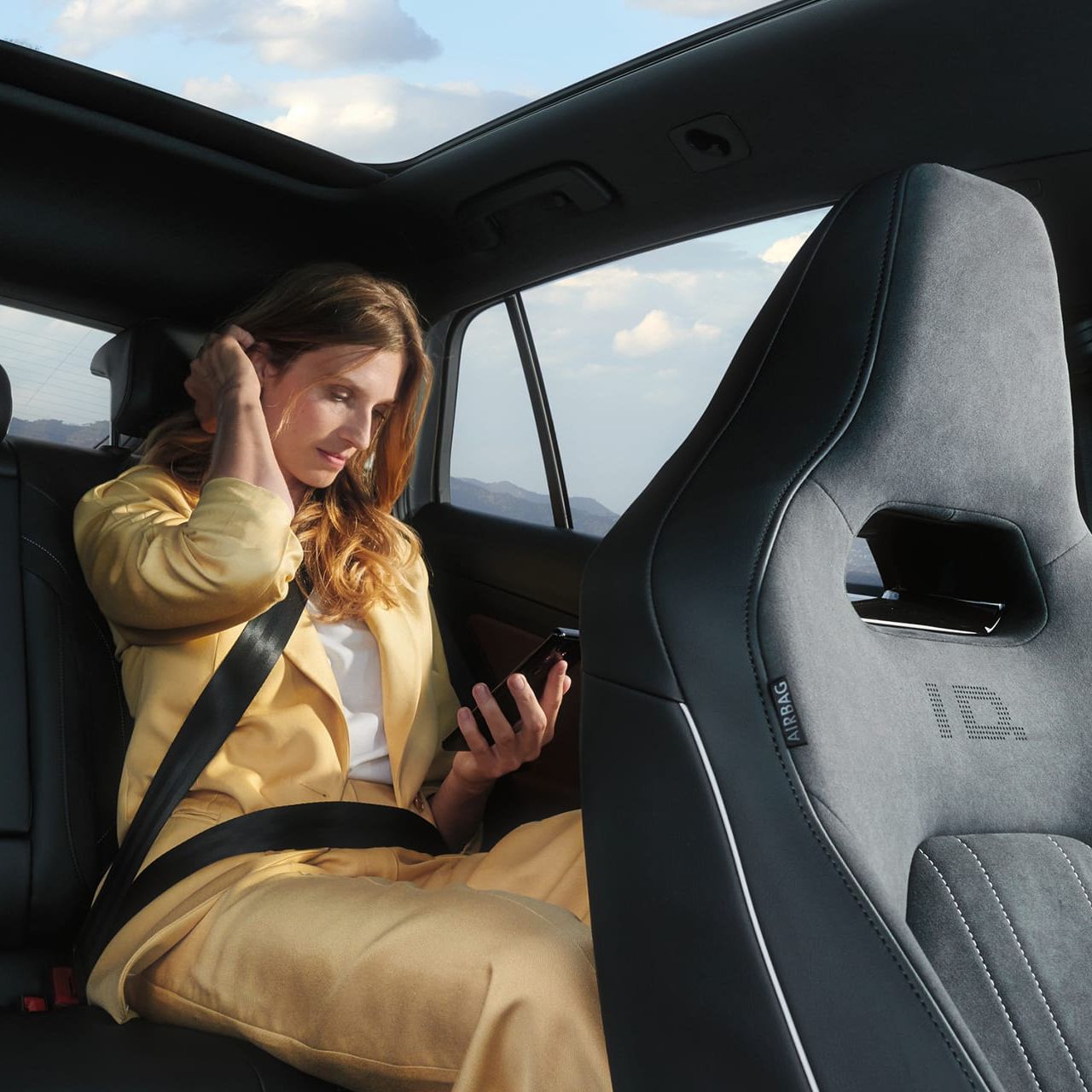 VW ID.5 Interieur, Blick auf die Rücksitzbank, Frau sitzt im Auto und schaut auf ihr Handy.