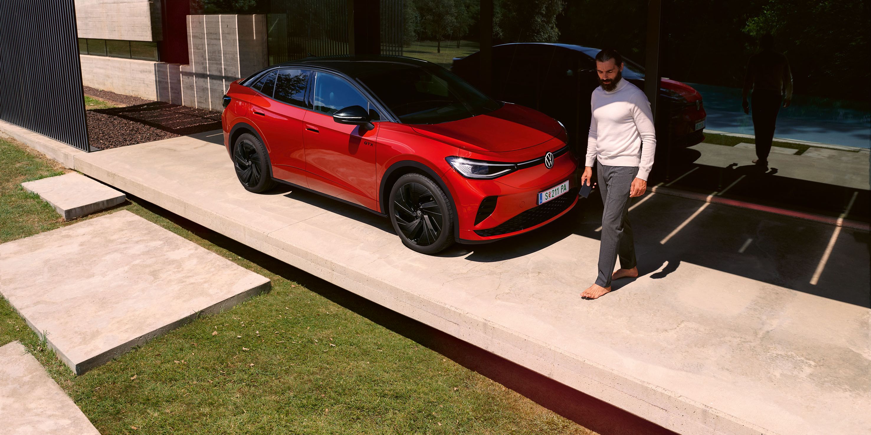 Roter VW ID.5 GTX von schräg vorne in einem modernen Carport, ein Mann geht vor der Motorhaube entlang