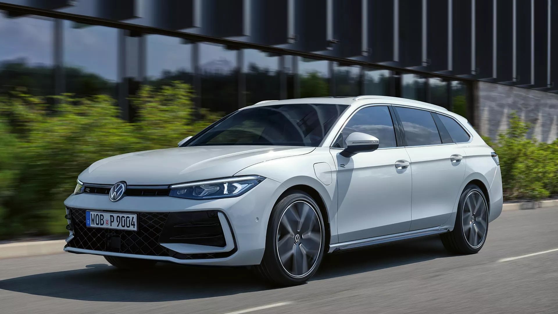 VW Passat in weiß fährt seitlich an einem Gebäude vorbei.